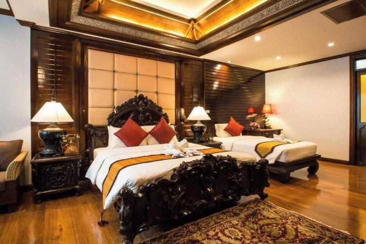 Een hotelkamer met twee bedden, een groot, versierd hoofdbord, een houten vloer en een kamerkleed met een patroon.