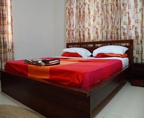A single bed with a wooden frame, red bedding, and a white pillow. - Calabash Green Executive Apartments (Accra)