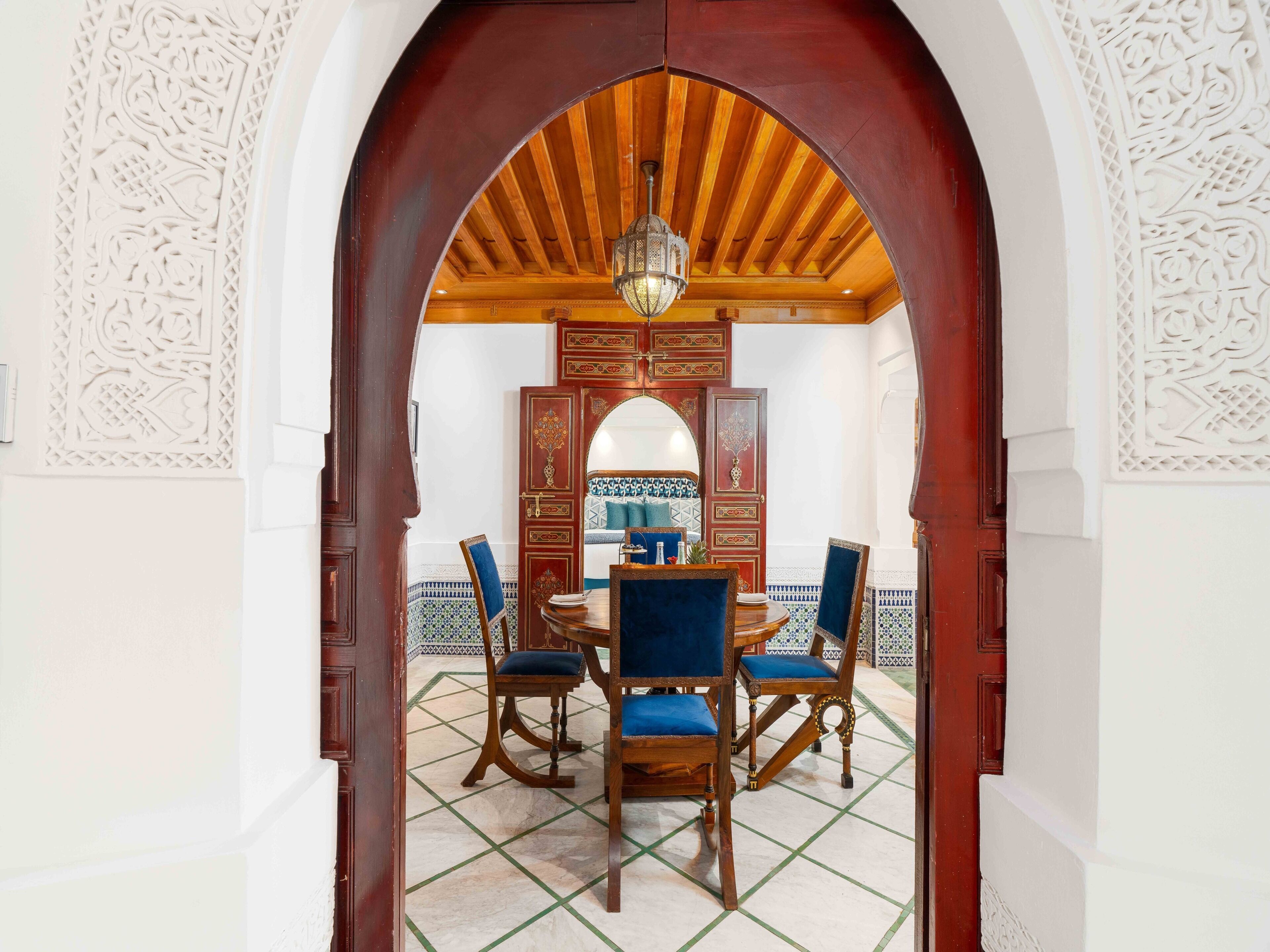 An arched doorway leading to a dining area with a wooden ceiling, patterned tiles, and traditional furniture.