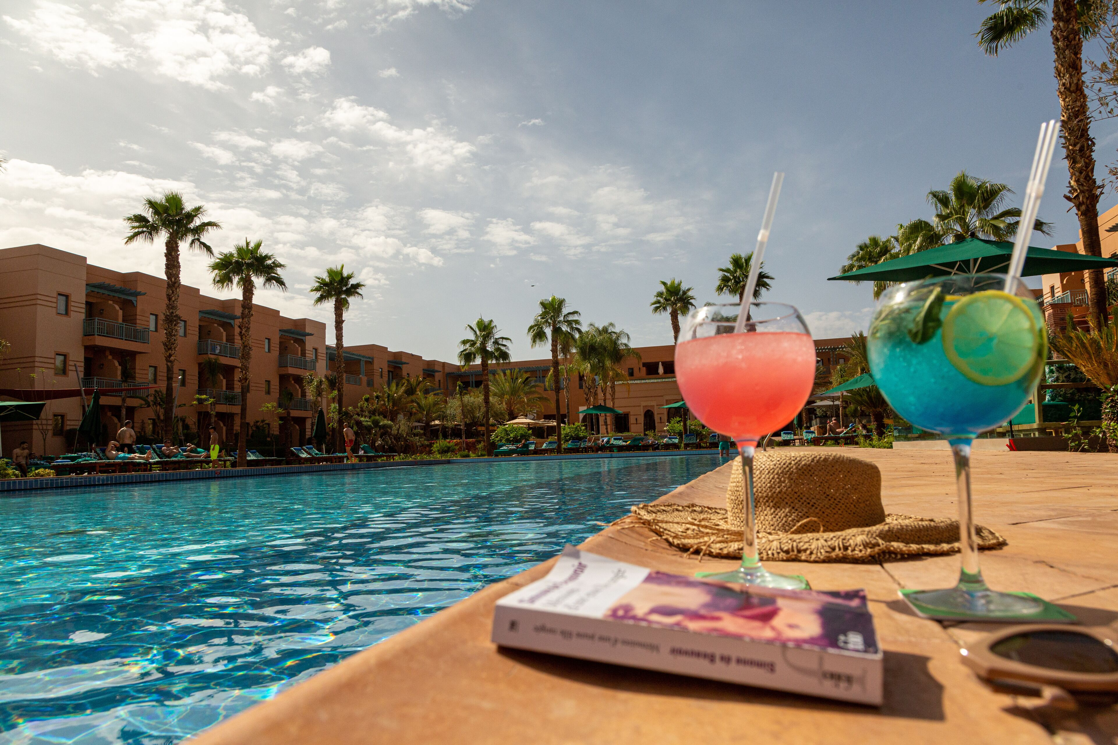 Zona piscina con due bevande, un libro e una lente d'ingrandimento su un tavolo.
