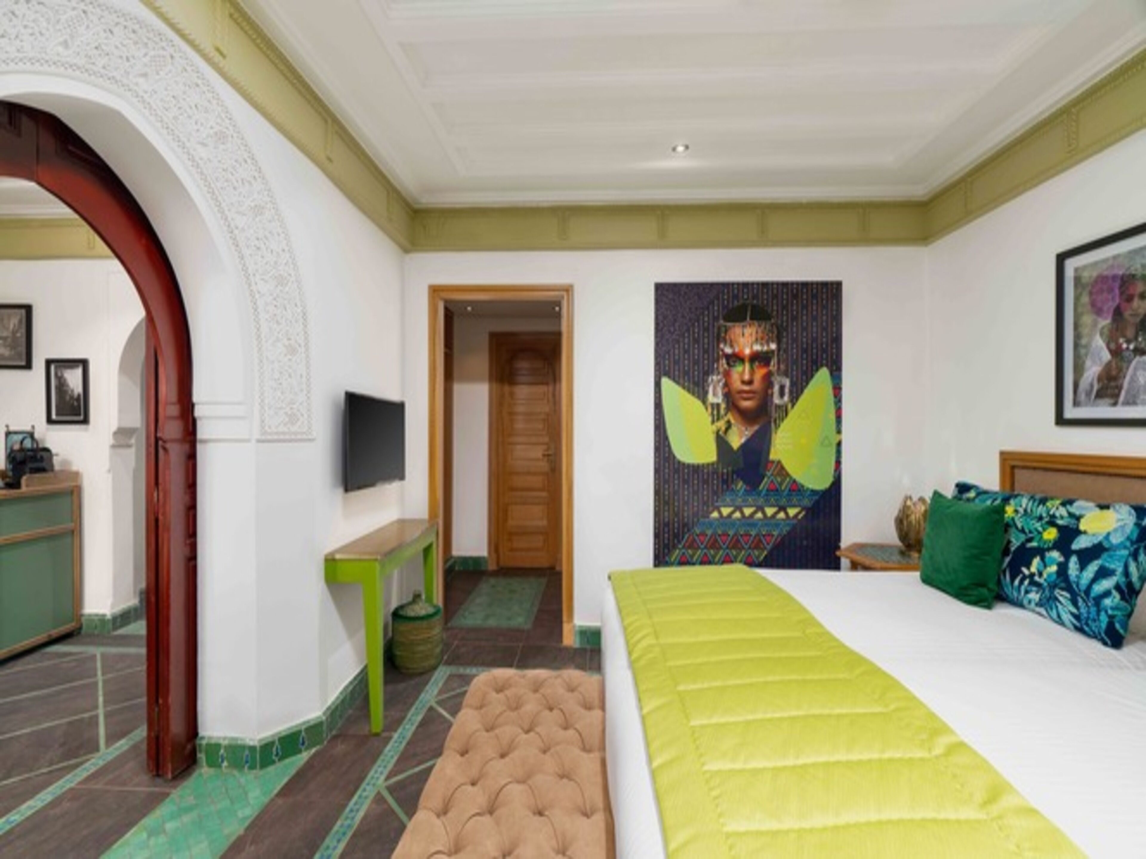 Une chambre à coucher avec un grand lit, une télévision, un bureau et une porte donnant sur une autre pièce.