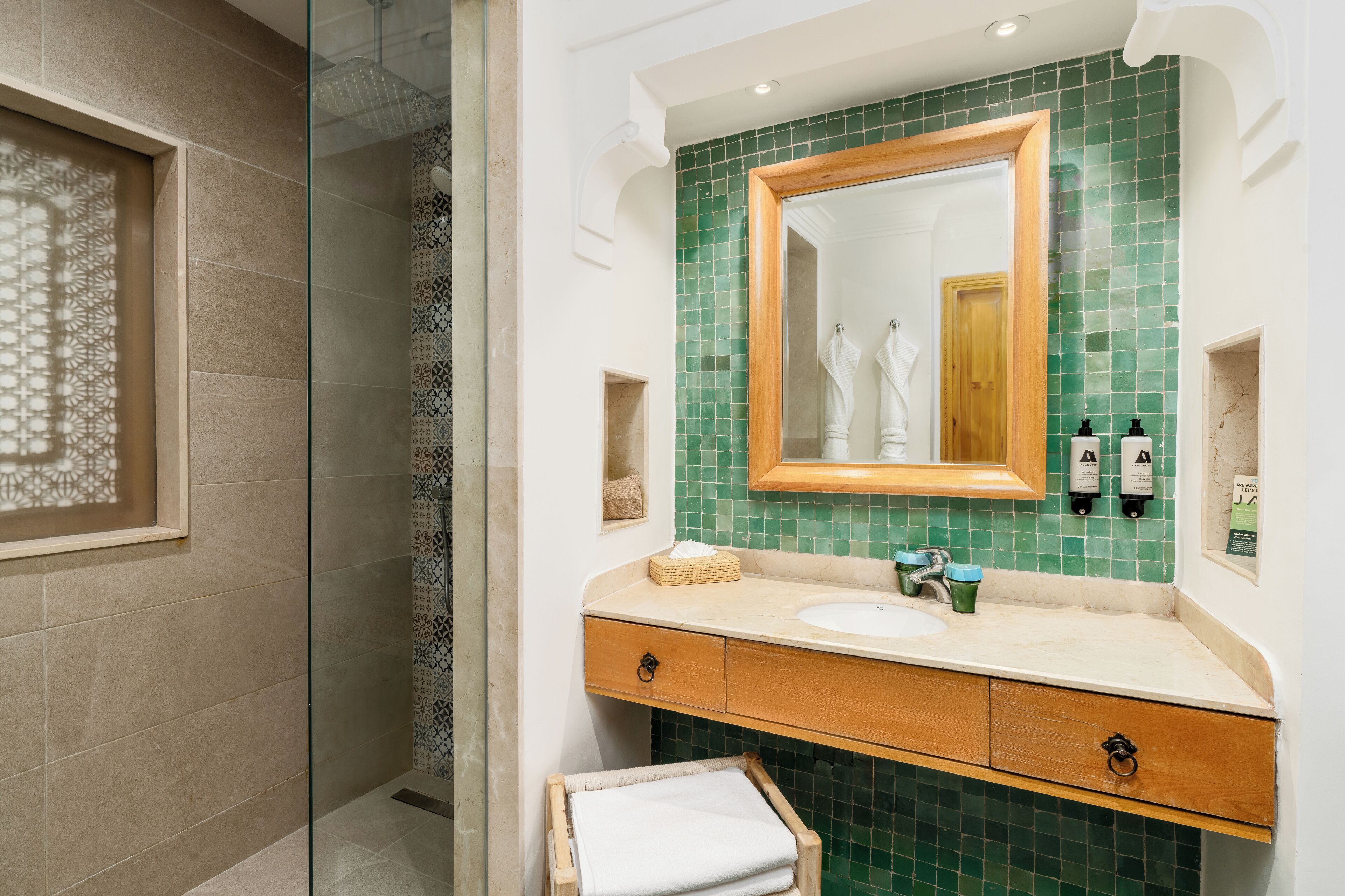 A bathroom with a glass shower enclosure, a wooden vanity with a green-tiled backsplash, and a large mirror.