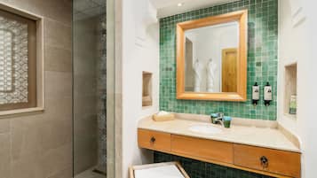 A bathroom with a glass shower enclosure, a wooden vanity with a green-tiled backsplash, and a large mirror.