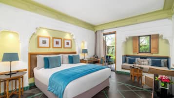A hotel room with a large bed, a desk with a lamp, a sofa, and a dining table.