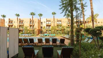 A poolside area with lounge chairs and a pool, surrounded by palm trees and a building with balconies.