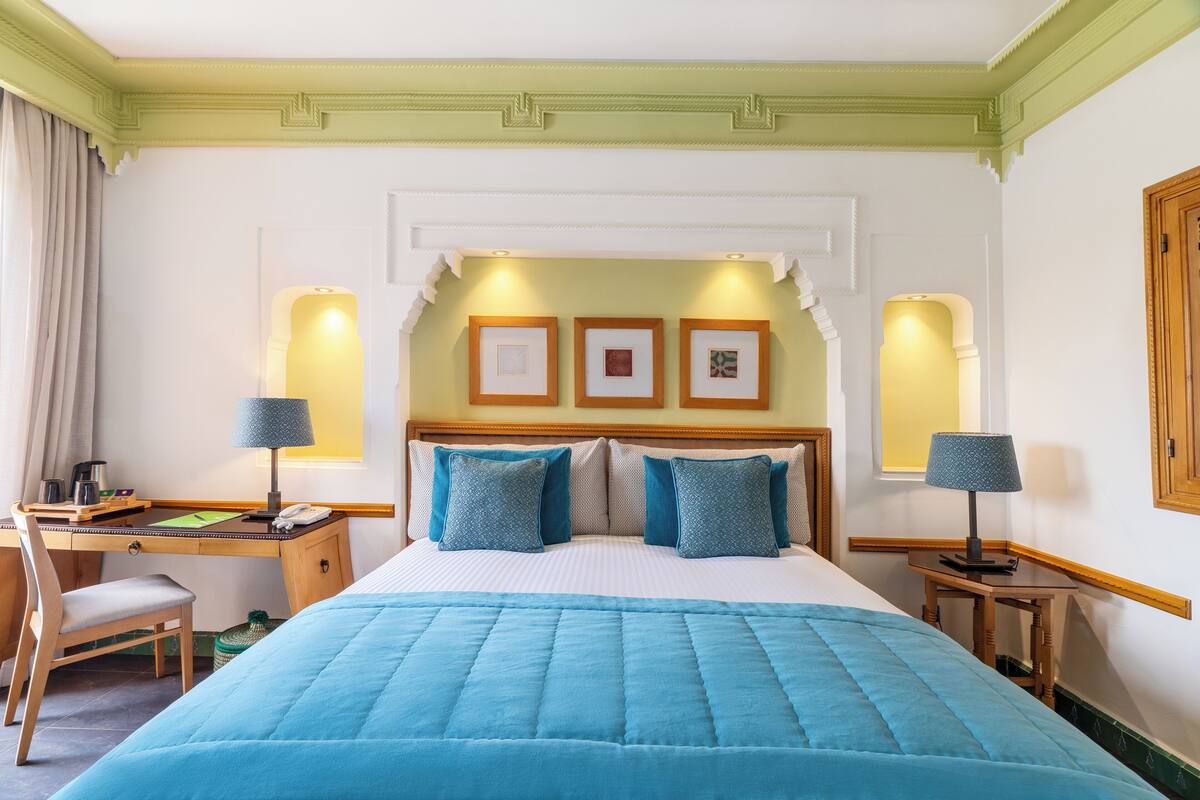 Une chambre d’hôtel comprenant un lit, un bureau, une chaise et deux lampes de chevet.