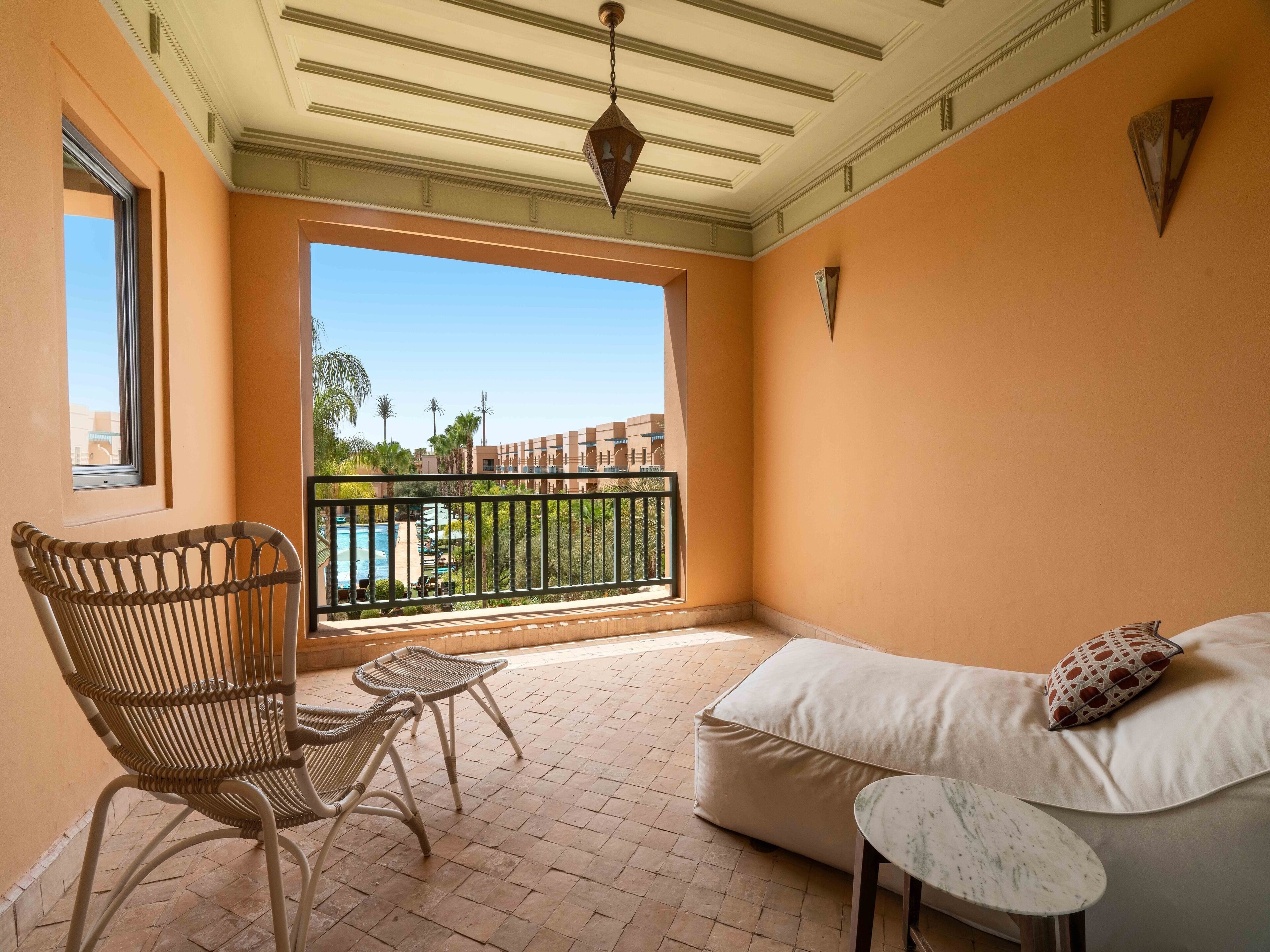 A balcony with a wicker chair, a small table, and a sofa with a pillow.