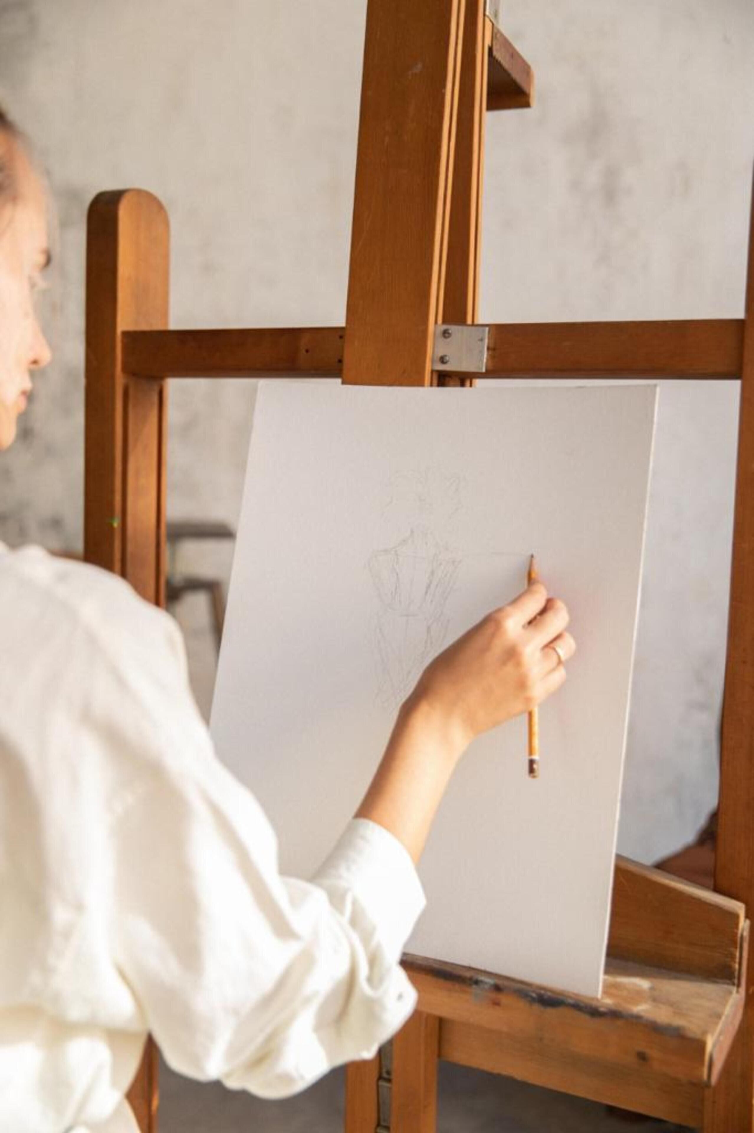 Eine Person malt auf einer weißen Leinwand, die an einem Holzeasel angebracht ist.