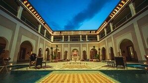 A spacious indoor pool area with a patterned floor, multiple seating areas, and a central fountain.
