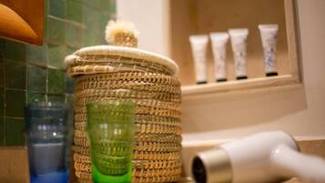 A bathroom counter with a woven basket, a green glass, a blue glass, and a white hairdryer.