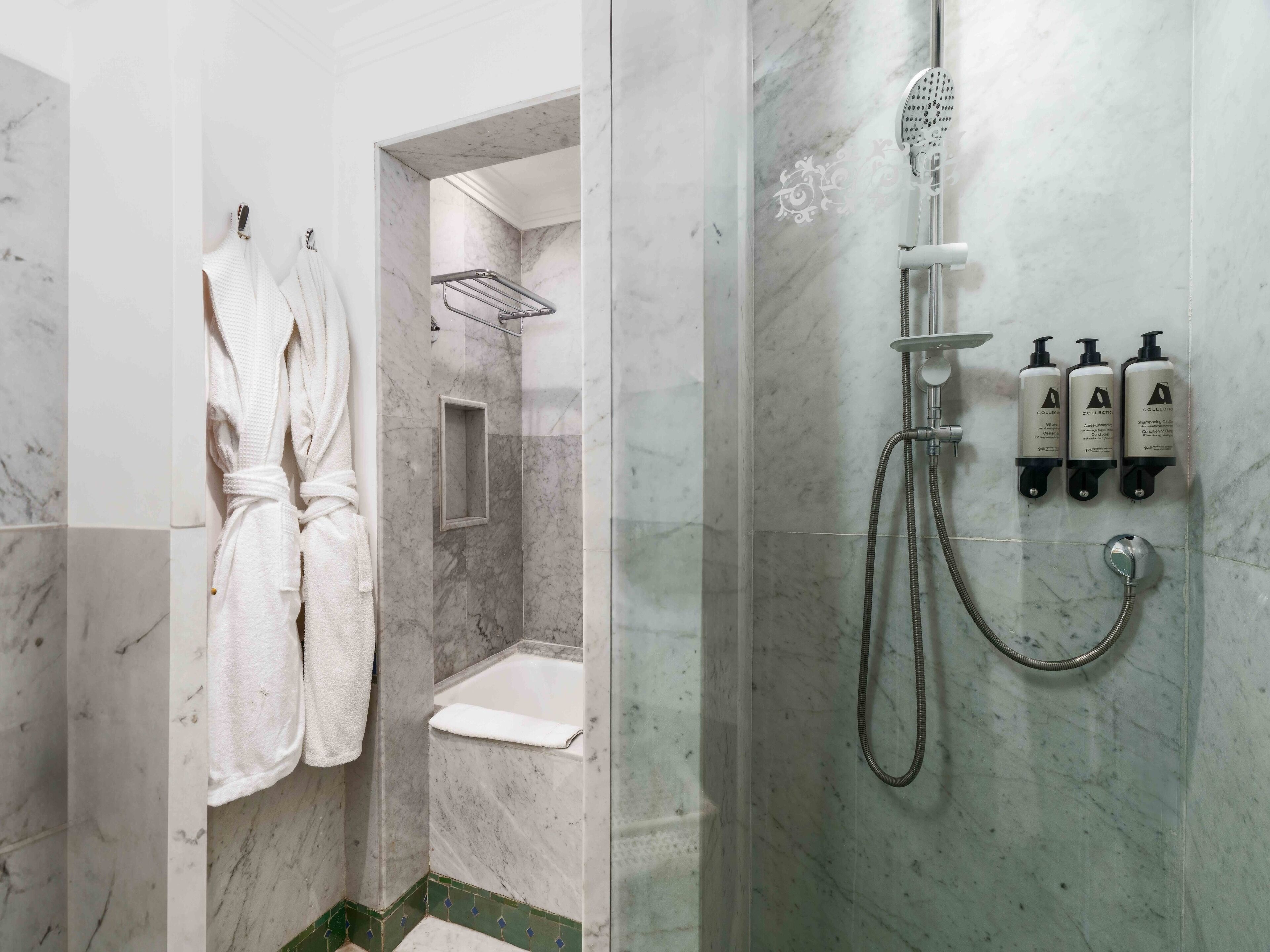 A bathroom with a shower, a bathtub, and a toilet. There are towels hanging on a rack and three bottles of shampoo on the wall.