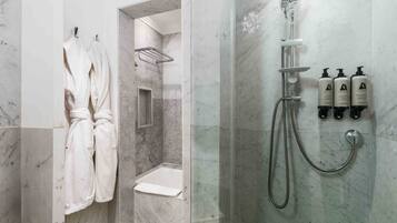 A bathroom with a shower, a bathtub, and a toilet. There are towels hanging on a rack and three bottles of shampoo on the wall.