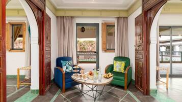 A room with a round table set for a meal, two armchairs, and a view through a window.