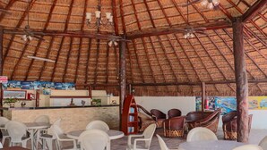 Un restaurante con techo de paja, varias mesas y sillas, y ventiladores de techo.
