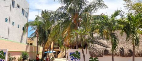 A resort entrance with palm trees, a sign for Villas Coco Resort Isla Mujeres, and a building with a thatched roof.