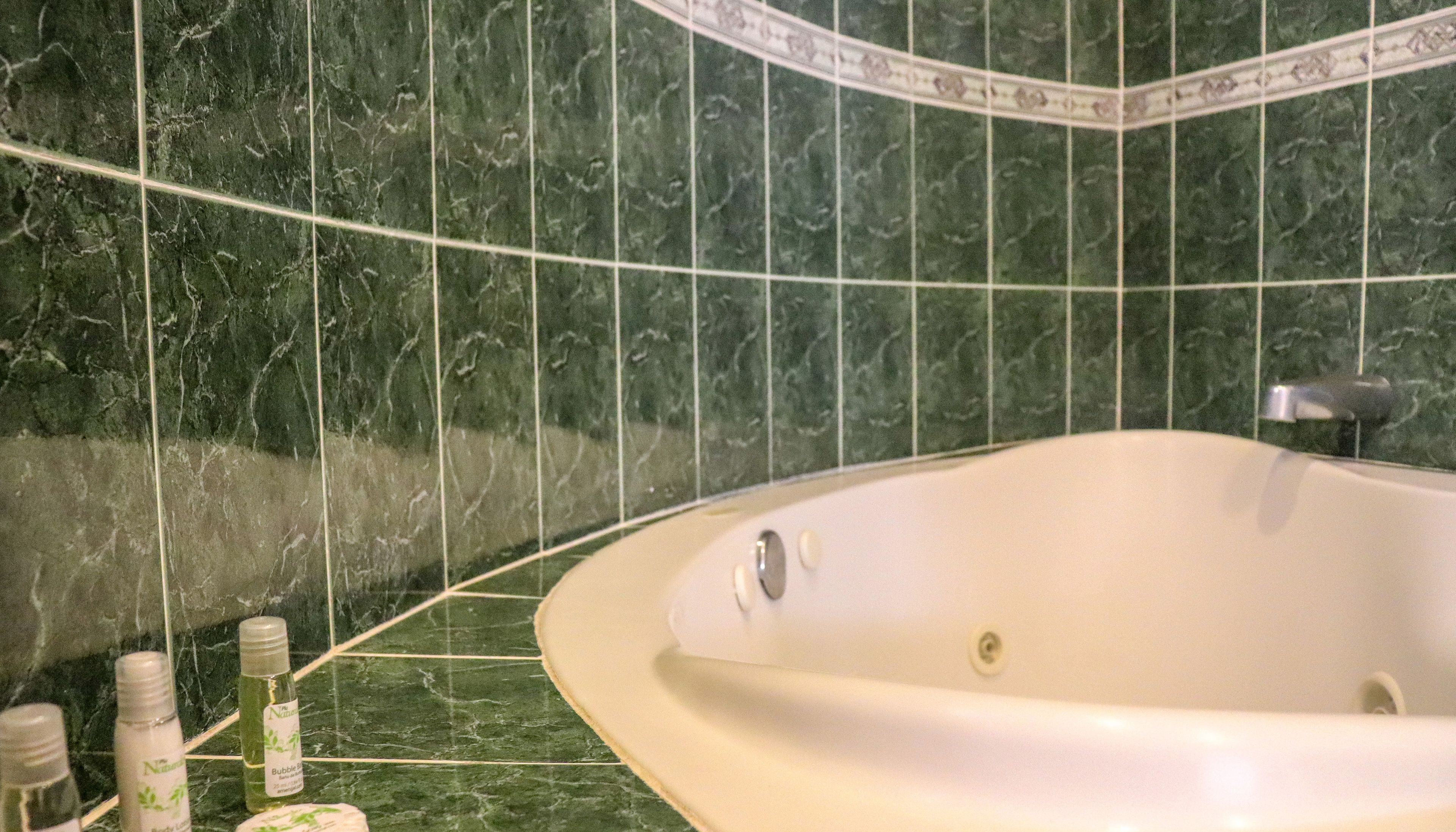 Un baño con una bañera independiente, baldosas de mármol verde y algunos artículos de tocador en la encimera.