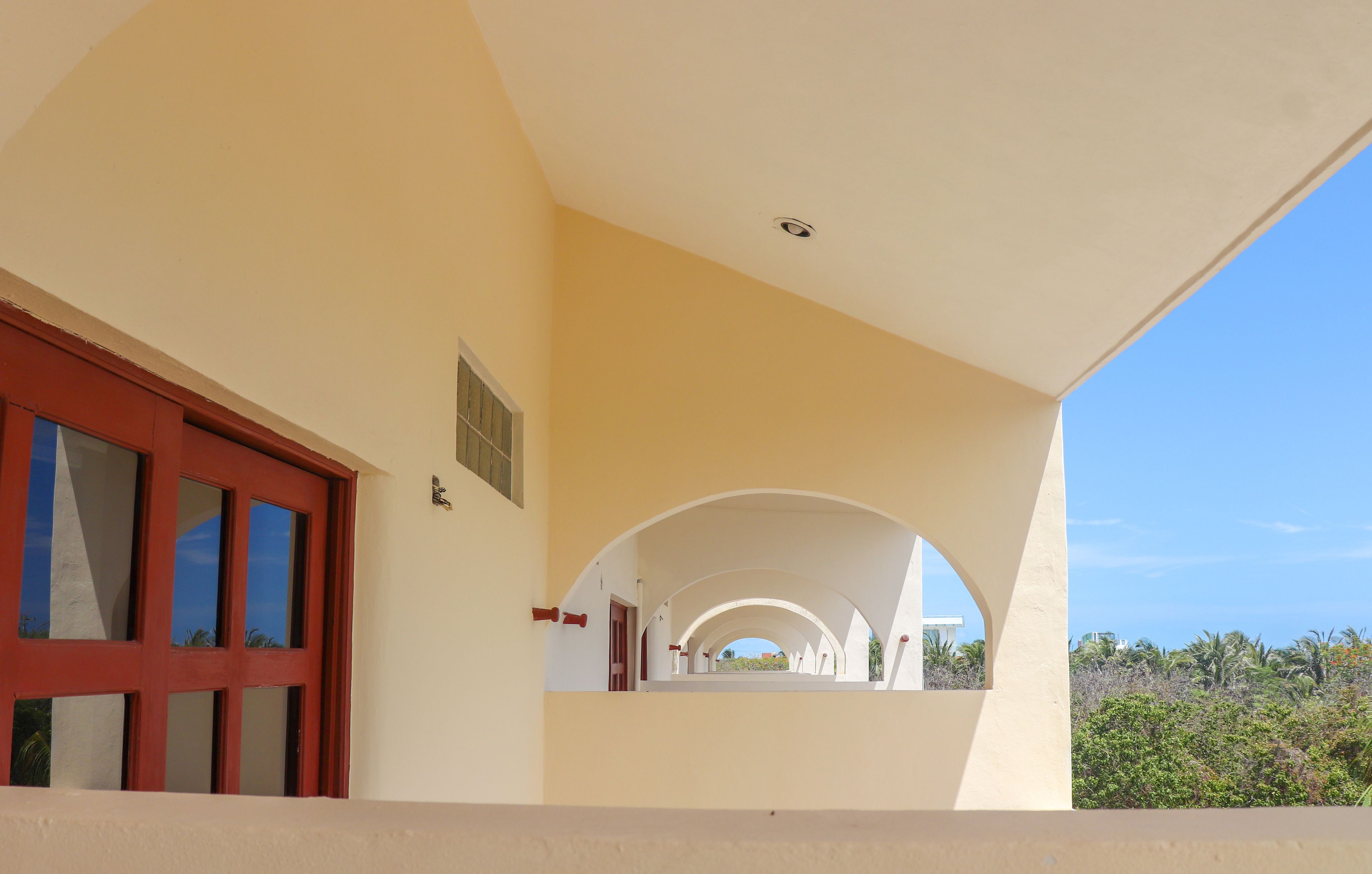 Un espacio al aire libre cubierto, con una puerta roja y arcos blancos.