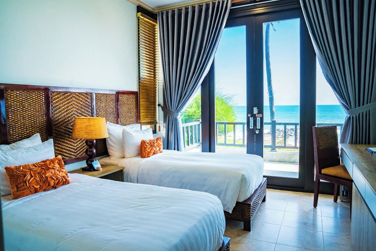 A hotel room with two beds, a nightstand, a lamp, and a view of the ocean.