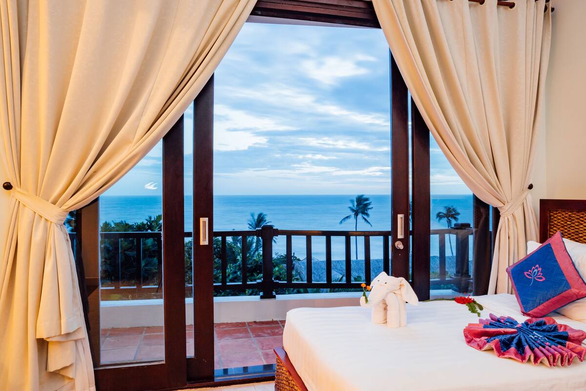 A hotel room with a balcony, a bed, and a view of the ocean.