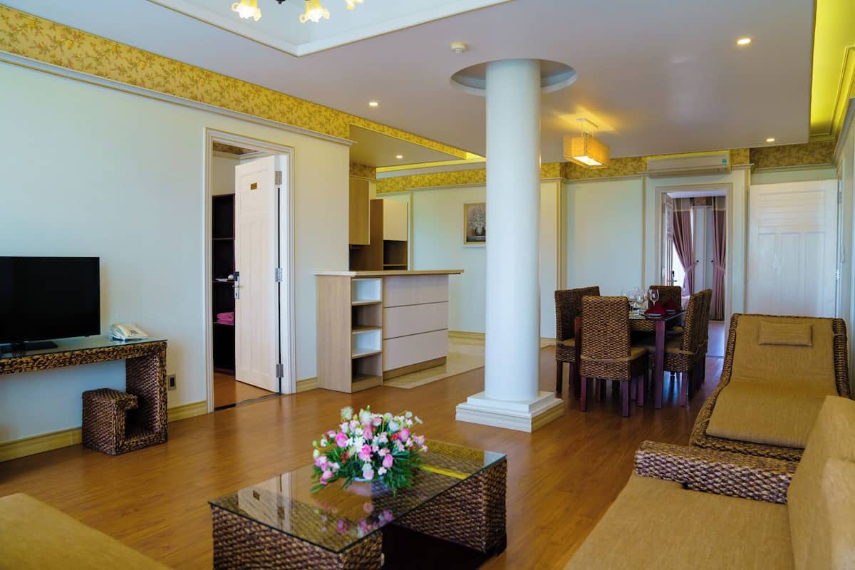 A spacious living room with a flat-screen TV, wicker furniture, a glass coffee table with flowers, and a dining area with wicker chairs.