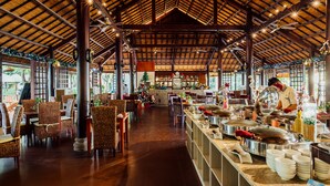 A spacious indoor area with a high ceiling and wooden beams, featuring a buffet setup with various food stations and seating arrangements. - Lotus Muine Resort & Spa (Phu Thuy)
