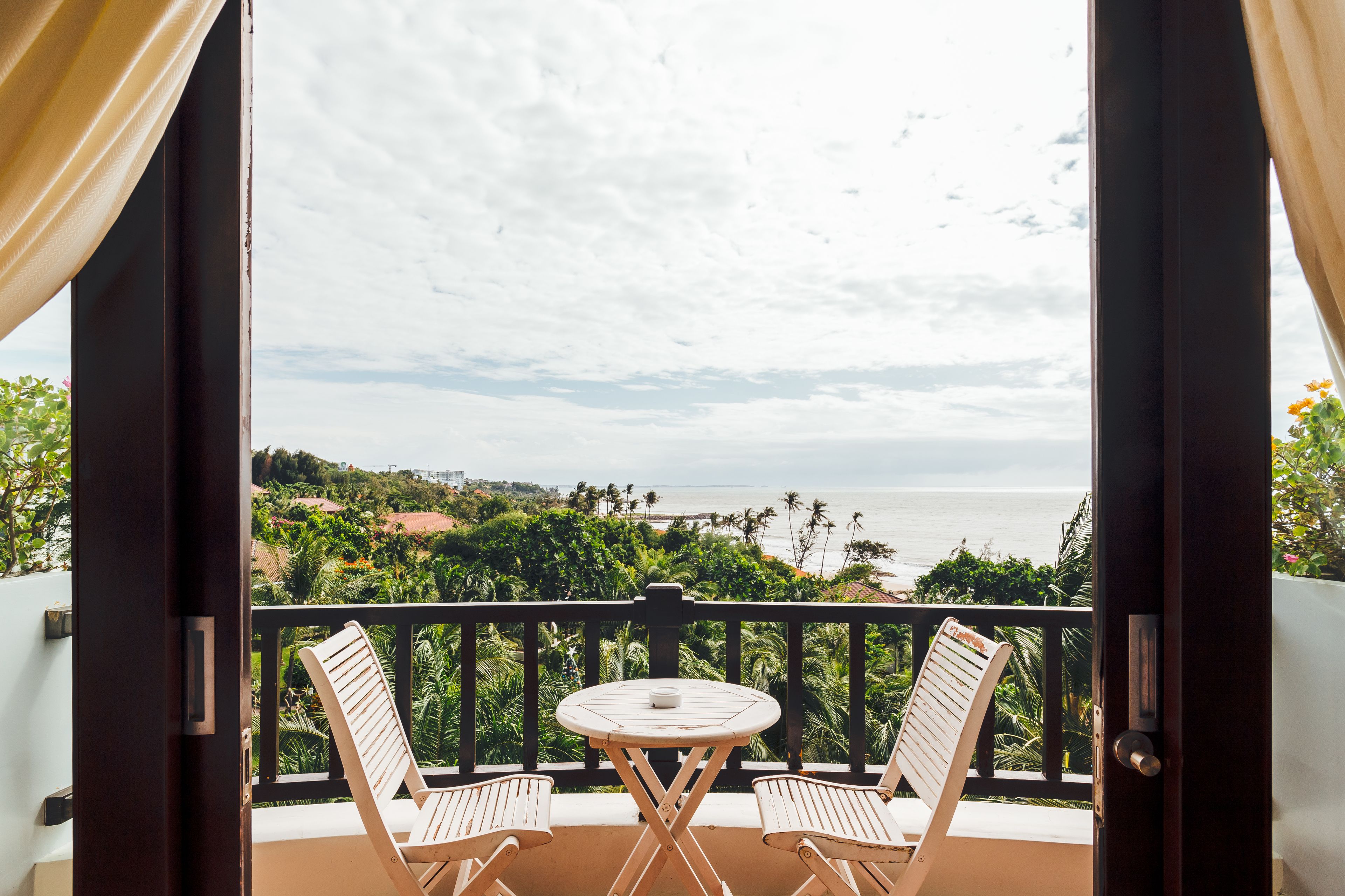 Varanda com duas cadeiras e uma mesa, com vista para a paisagem costeira com palmeiras e o oceano.