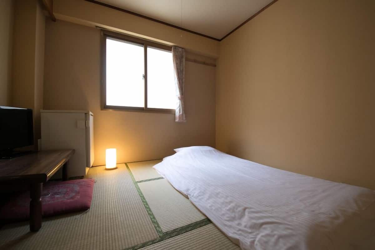 Une pièce comprenant un lit, un bureau, une lampe et une fenêtre avec un rideau.