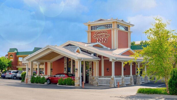 A Grand Country Inn with a prominent red and beige facade, a covered front porch, and a parking lot with several cars. - Grand Country Waterpark Resort (Branson)
