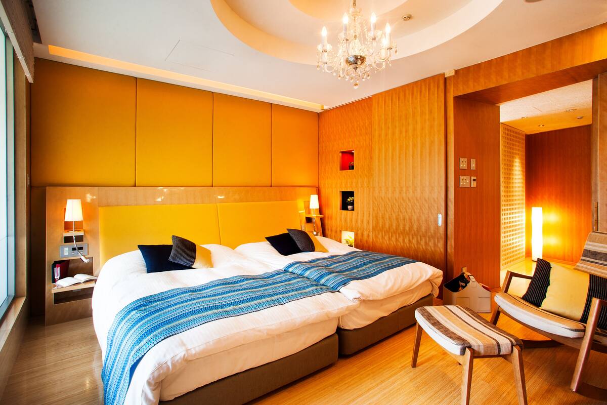A hotel room with a large bed, bedside tables, a chair, and a chandelier.
