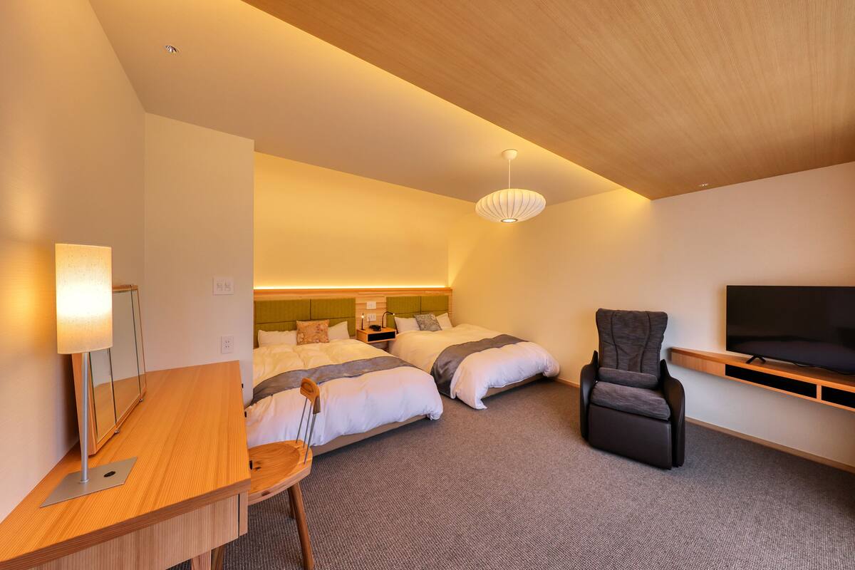 Ein Hotelzimmer mit zwei Betten, einem Schreibtisch, einem Stuhl, einem Fernseher und einer Deckenleuchte.