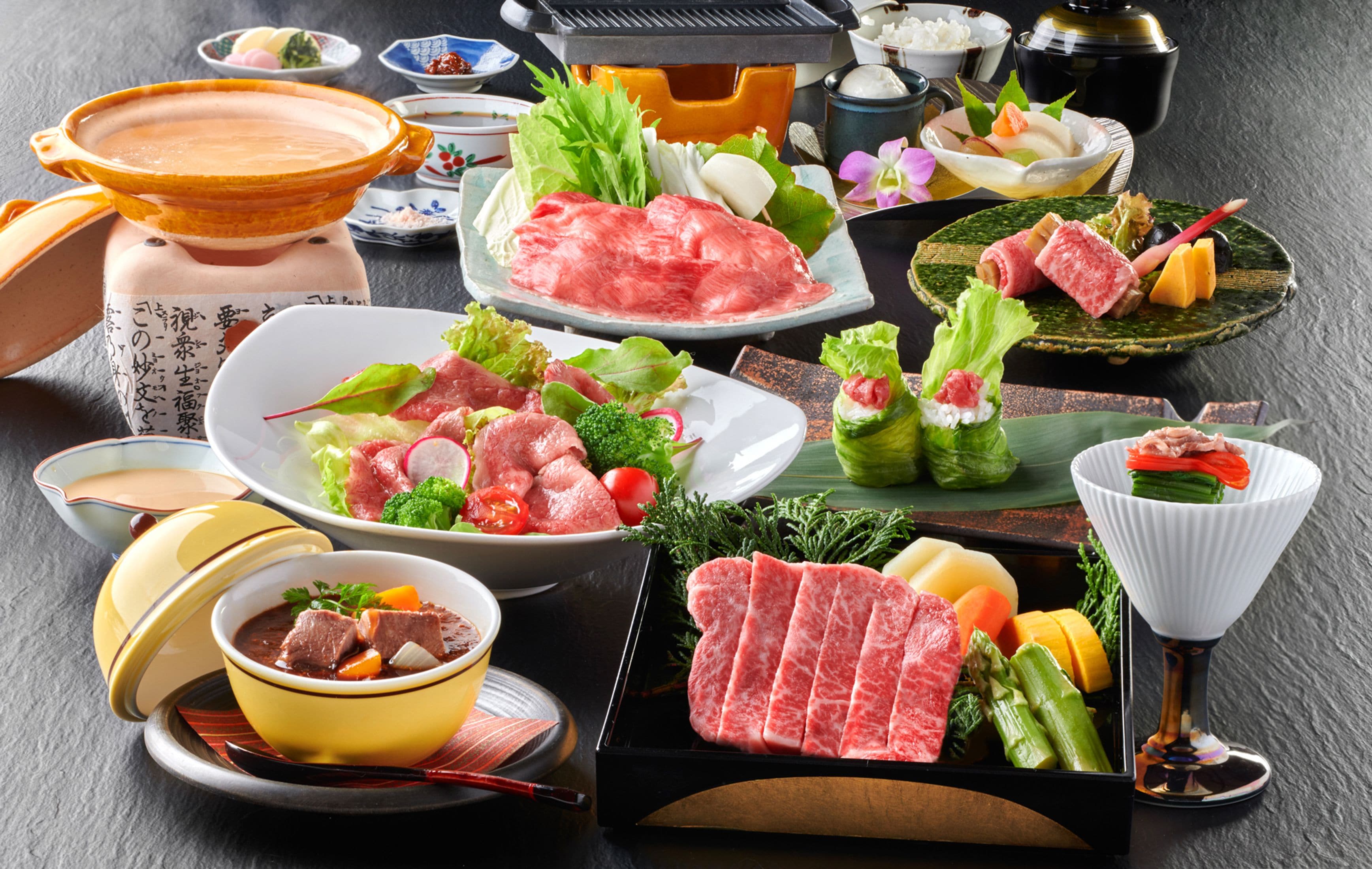 A variety of Japanese dishes including sashimi, vegetables, and a hot pot setup.