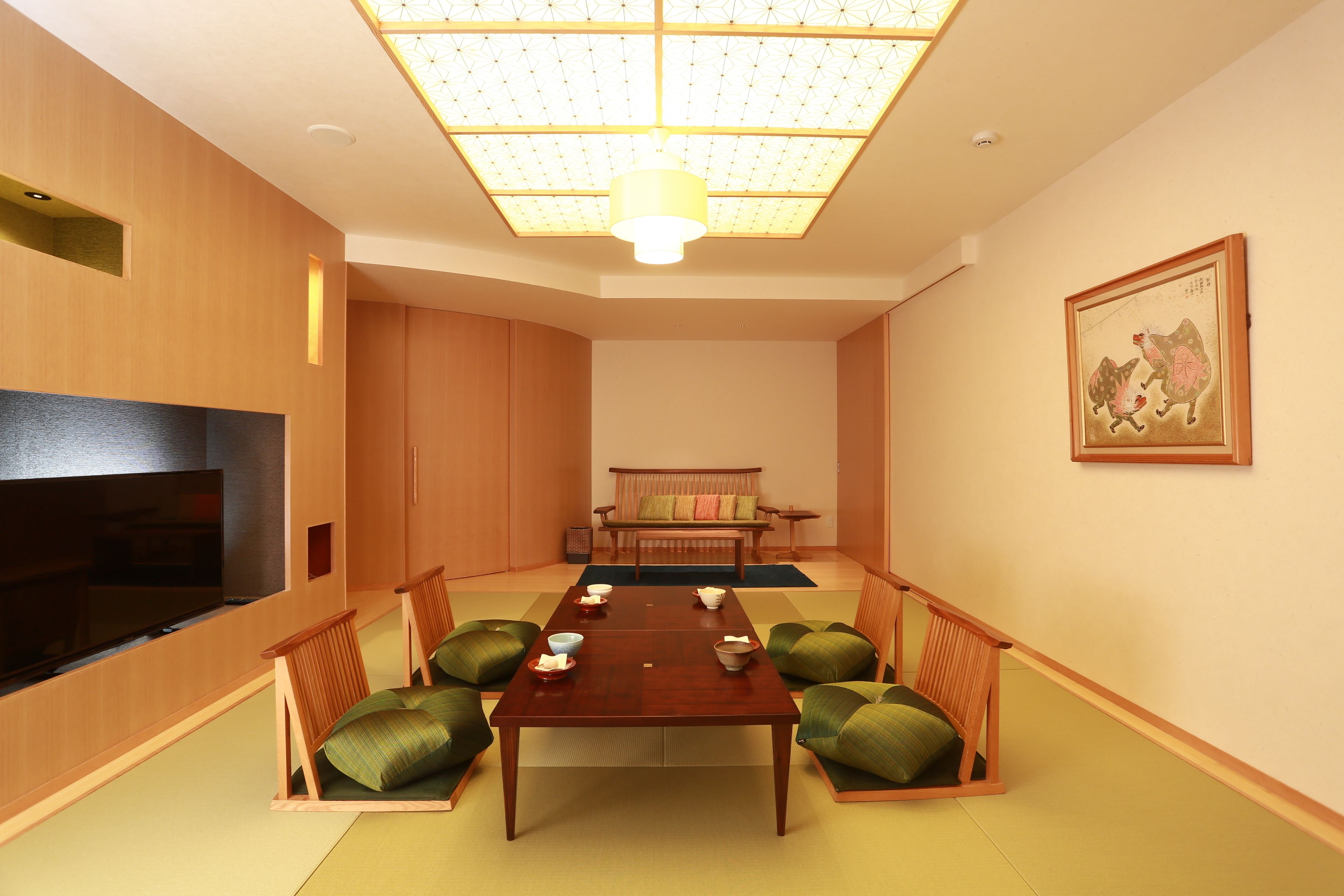 Quarto japonês tradicional com tatames, uma mesa baixa com almofadas, televisão e luminária no teto.