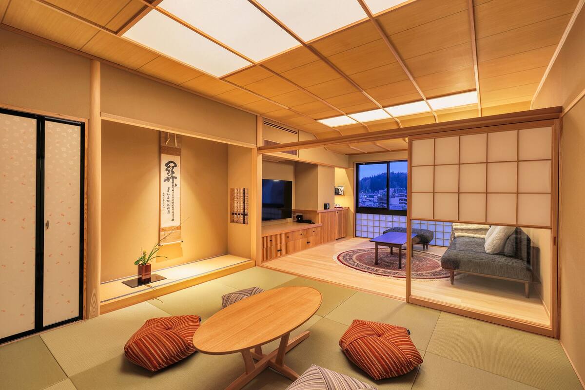 Ein traditioneller japanischer Raum mit Tatami-Boden, einem niedrigen Tisch, Kissen, einer Schiebetür und Blick auf eine verschneite Landschaft.
