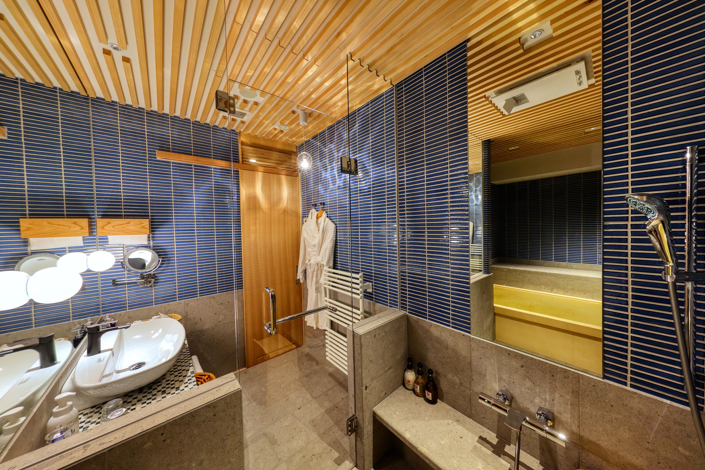 A modern bathroom with a wooden ceiling, a large mirror, a sink, and a bathtub.