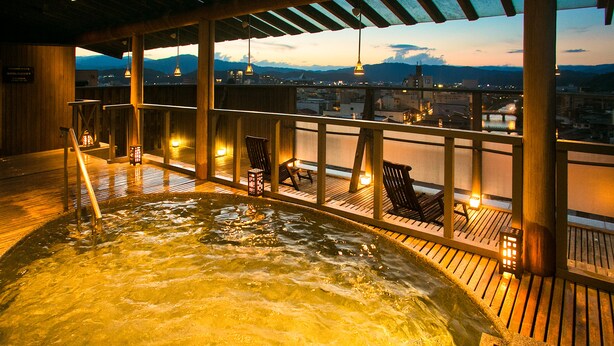 Ein Whirlpool mit Holzboden und Stühlen mit Blick auf eine Stadtlandschaft im Dämmerlicht.