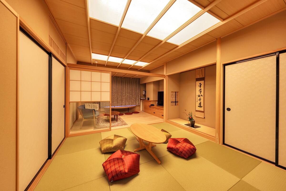 Ein traditioneller japanischer Raum mit Tatami-Böden, einem niedrigen Tisch, Kissen, Schiebetüren und einer Decke mit Oberlichtern.