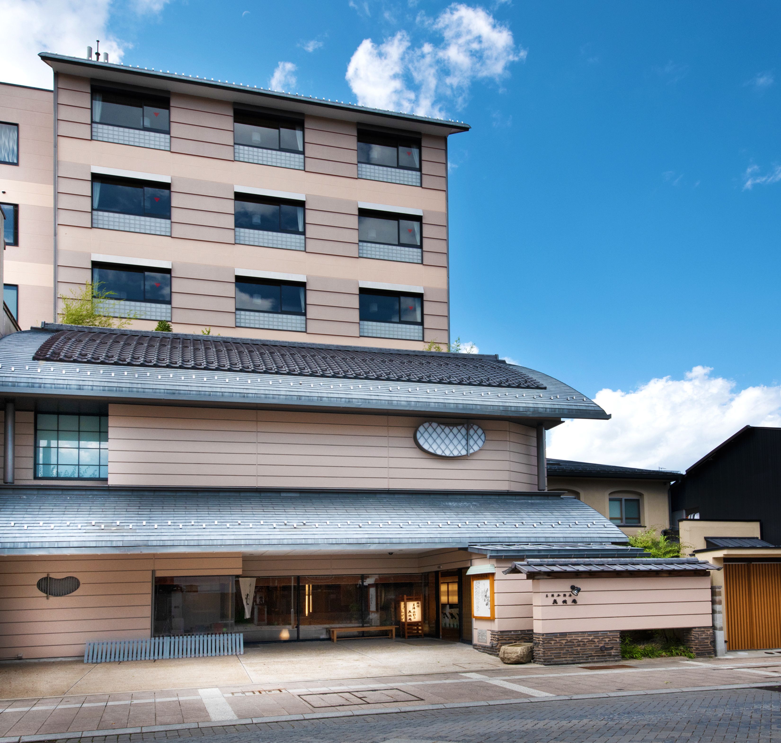 A multi-story hotel with a traditional tiled roof, large windows, and a covered entrance area with a bench.