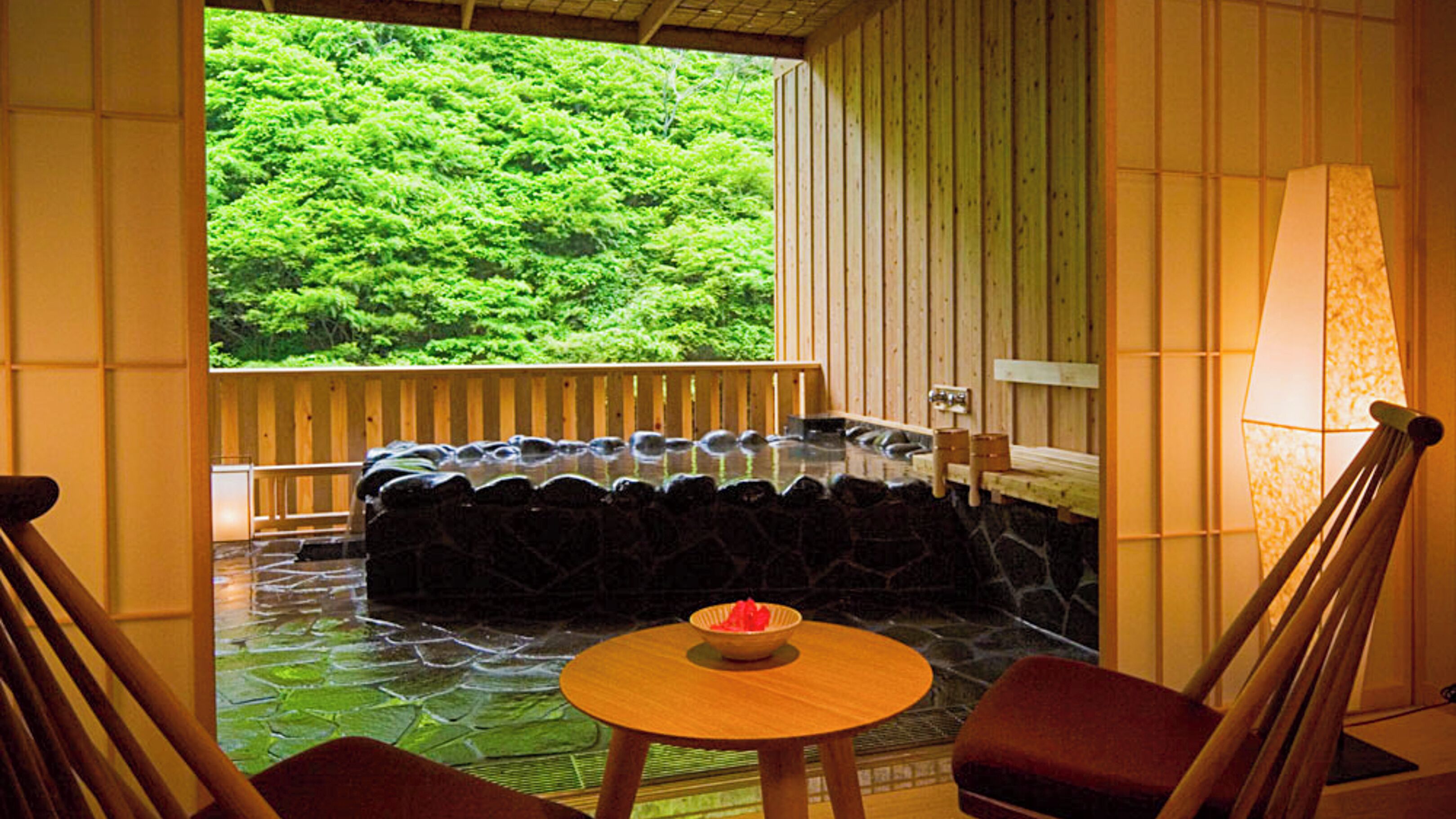 A traditional Japanese onsen with a stone hot spring, wooden benches, and a view of lush greenery.