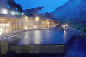 Un spa con piscina climatizada al aire libre, estructuras de madera y un paisaje montañoso de fondo.
