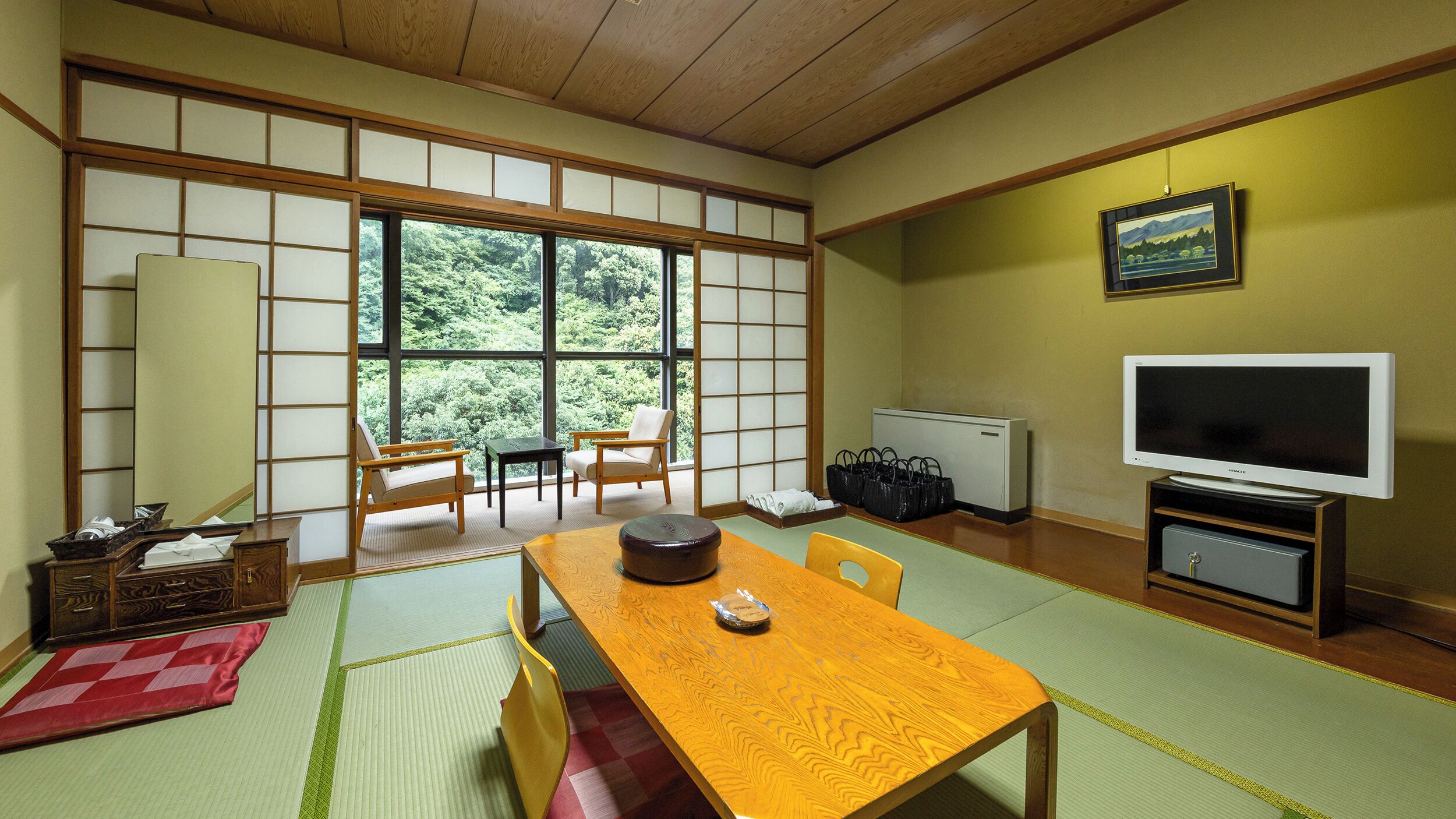 A traditional Japanese-style room with tatami flooring, a low table, a sofa, and a TV.