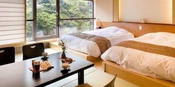 A hotel room with two beds, a dining table with coffee cups, and a view of greenery through the window.
