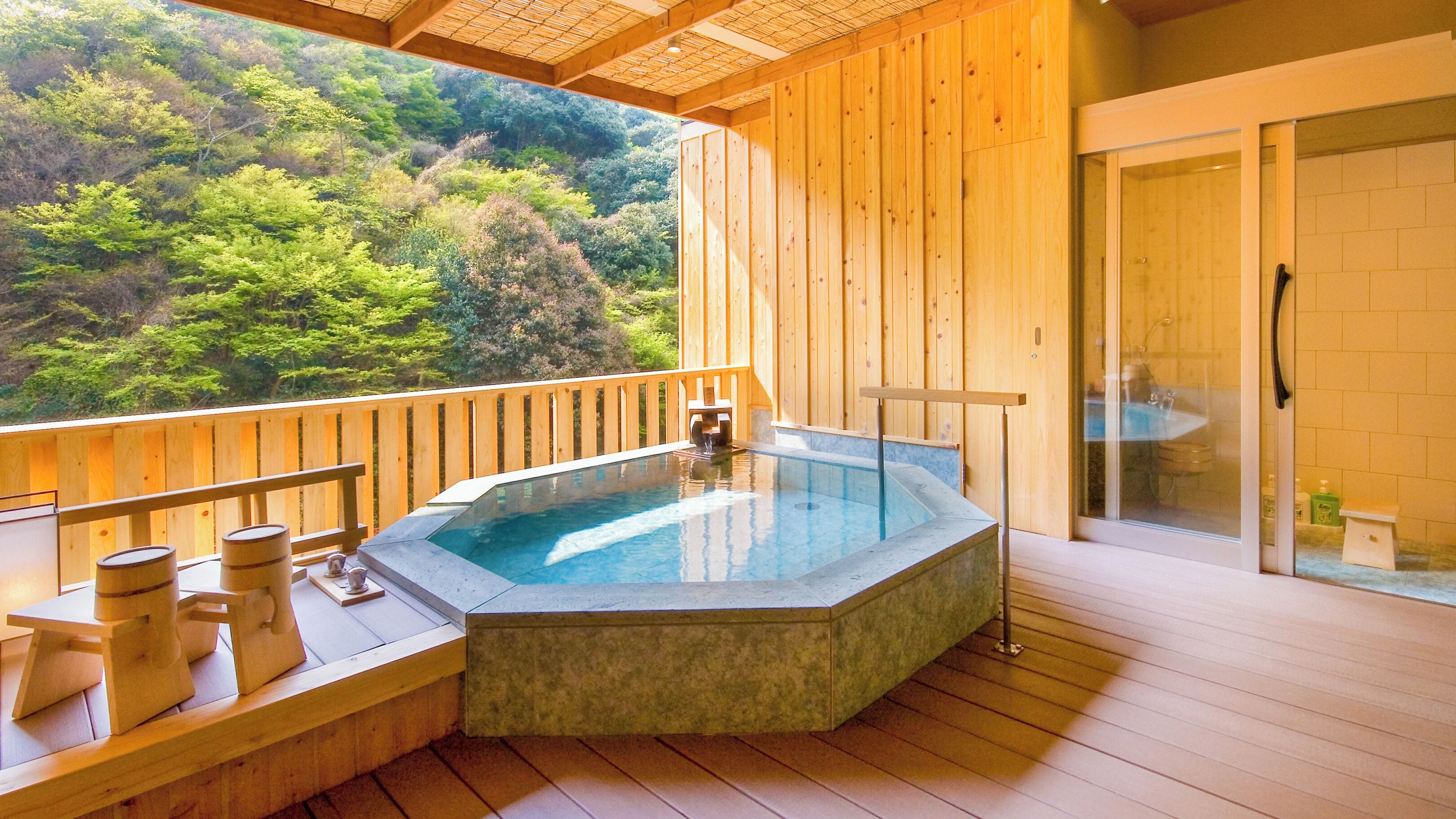 Terraza de madera con jacuzzi, barandas de madera y zona de ducha con cerramientos de vidrio.