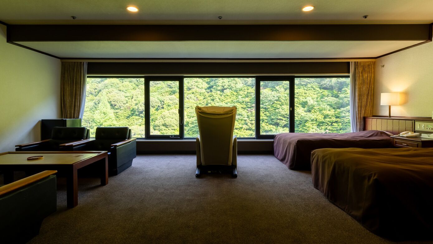 A hotel room with a large window, a desk, two beds, and a chair.