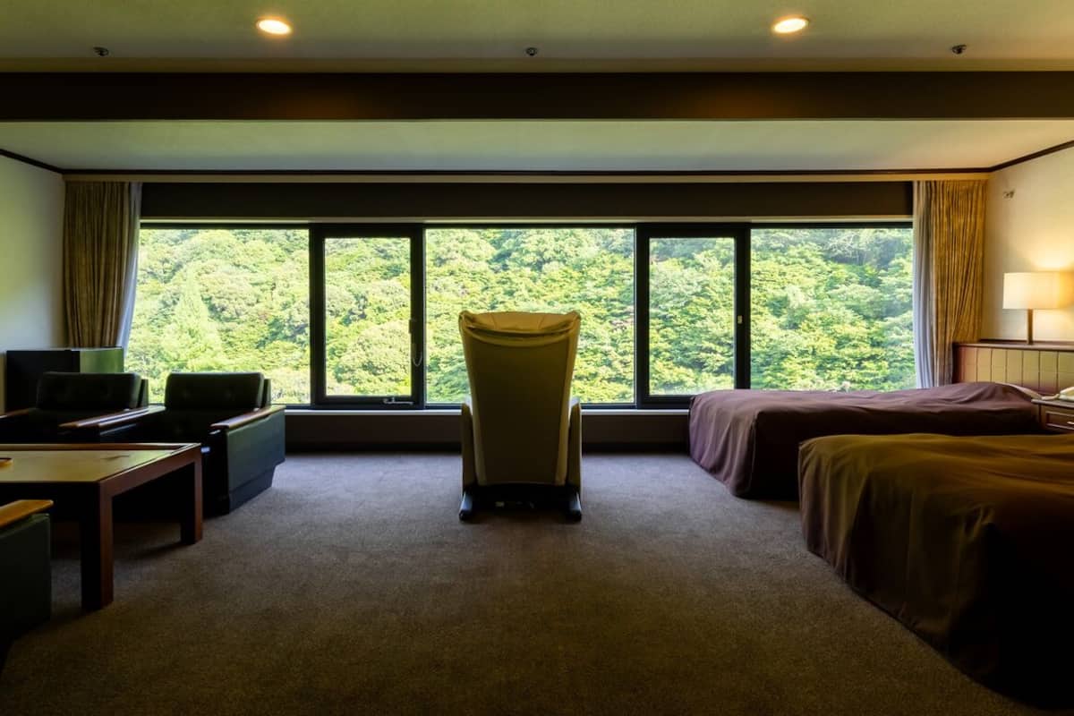 Una habitación de hotel con un ventanal grande, un escritorio, dos camas y una silla.