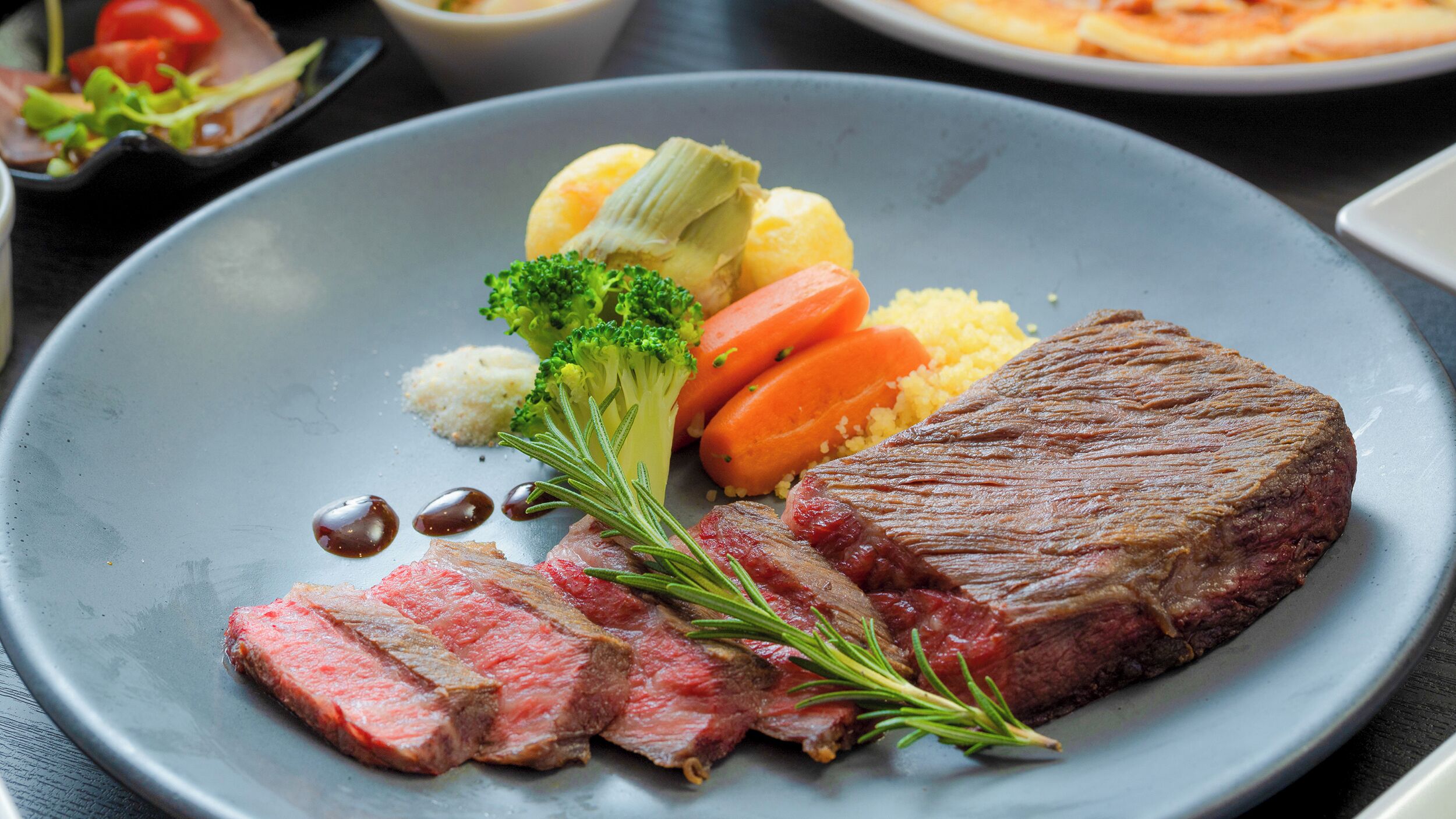 A plate with steak, broccoli, carrots, and couscous.