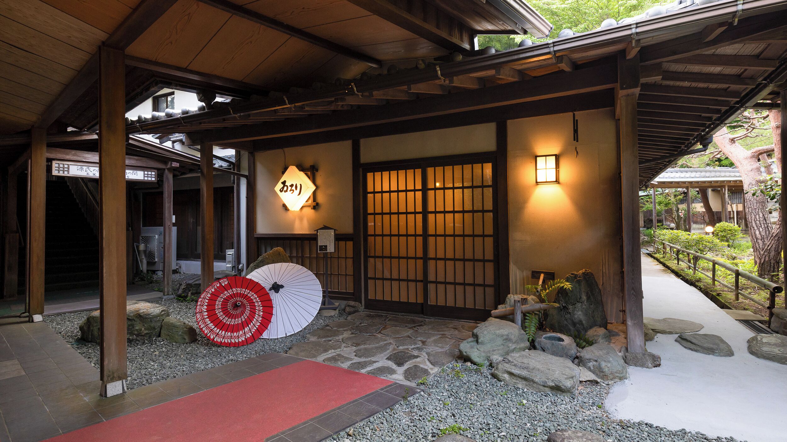 Un edificio japonés tradicional con estructura de madera, un camino de piedra y un tapete rojo que conduce a la entrada.