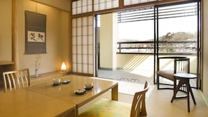 Een traditionele Japanse kamer met tatami vloeren, een lage tafel met een theeservies en een schuifdeur die uitkomt op een balkon met uitzicht op gebouwen.