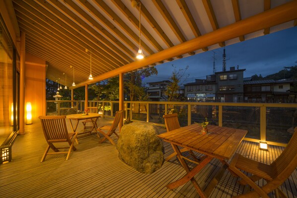Une terrasse en bois avec une table et des chaises, un grand rocher et, en arrière-plan, une vue sur des bâtiments.