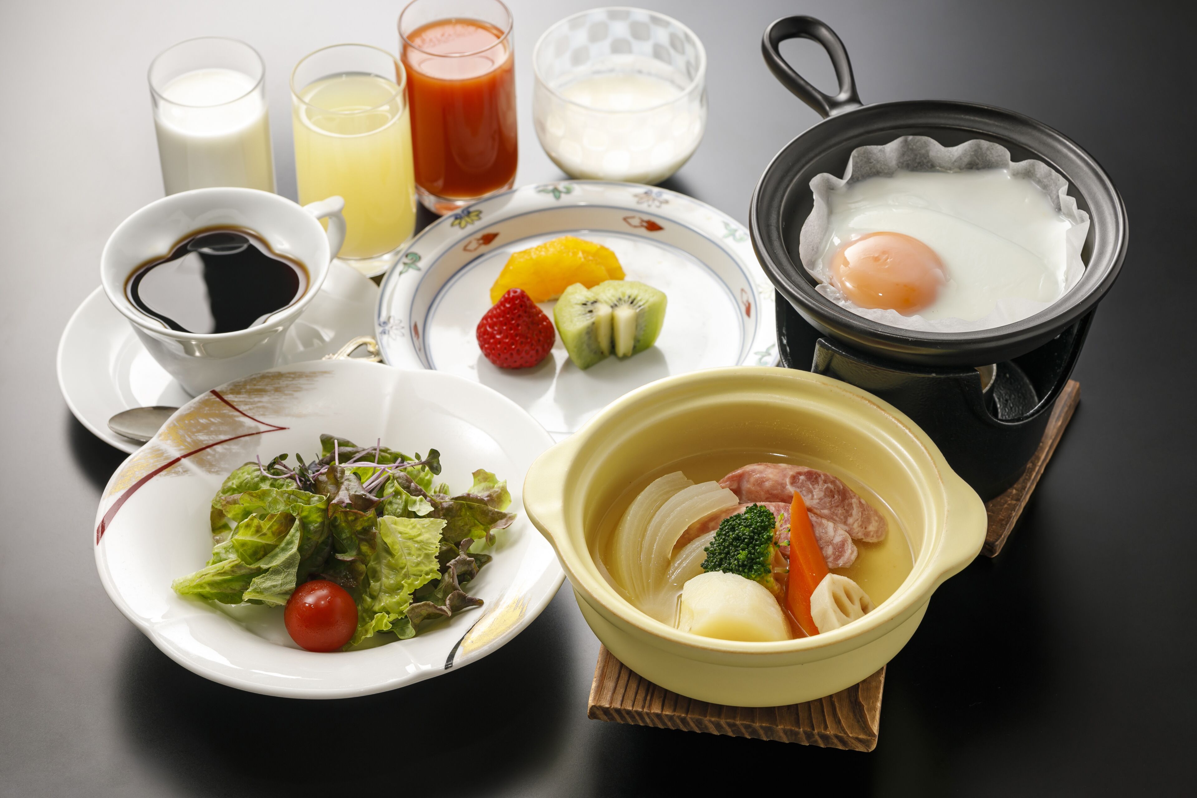 A breakfast setting with a variety of food items including eggs, fruits, vegetables, and beverages.