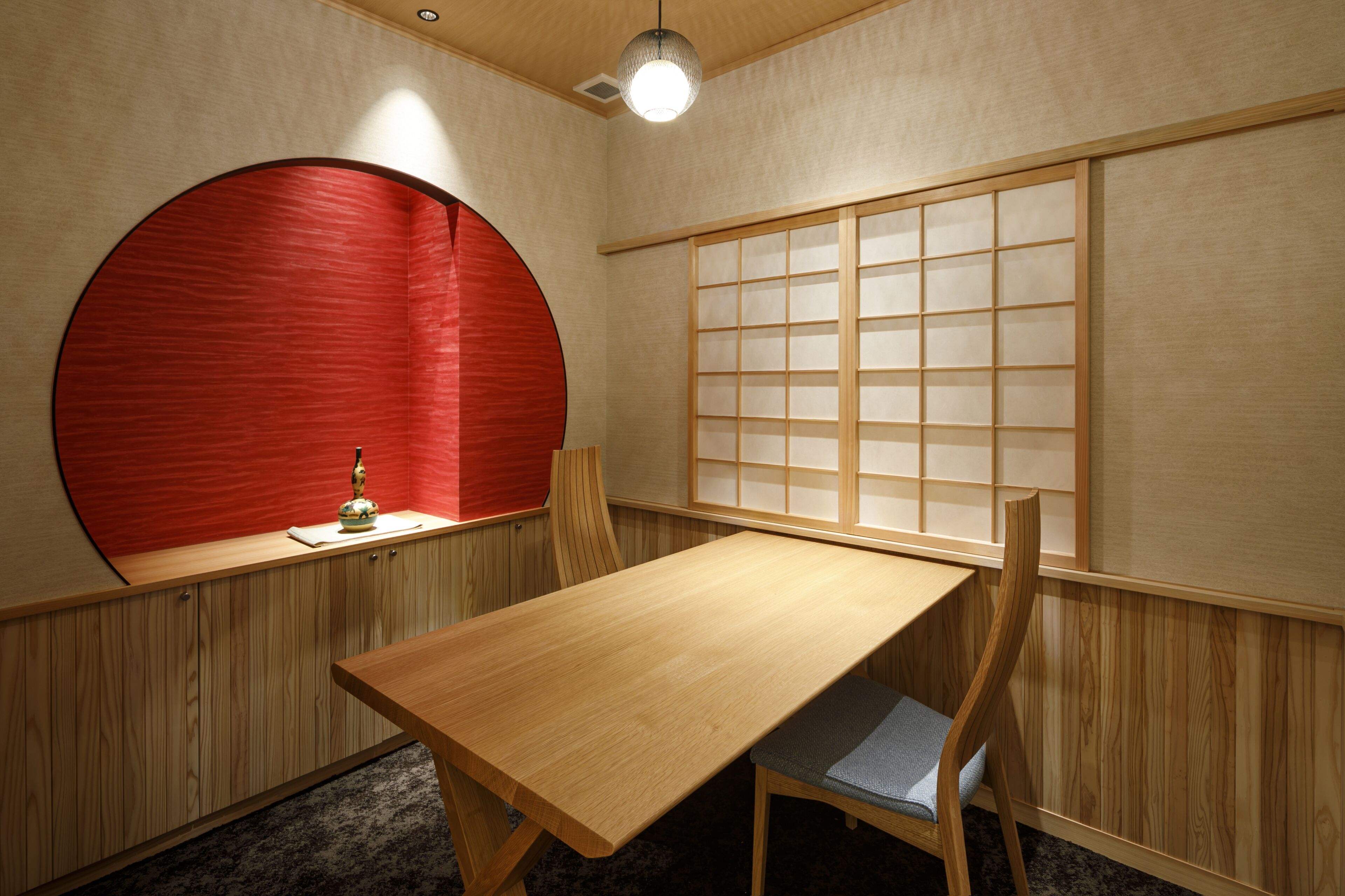 Una habitación con una mesa de madera, una silla, un panel de pared circular rojo y un fusuma.